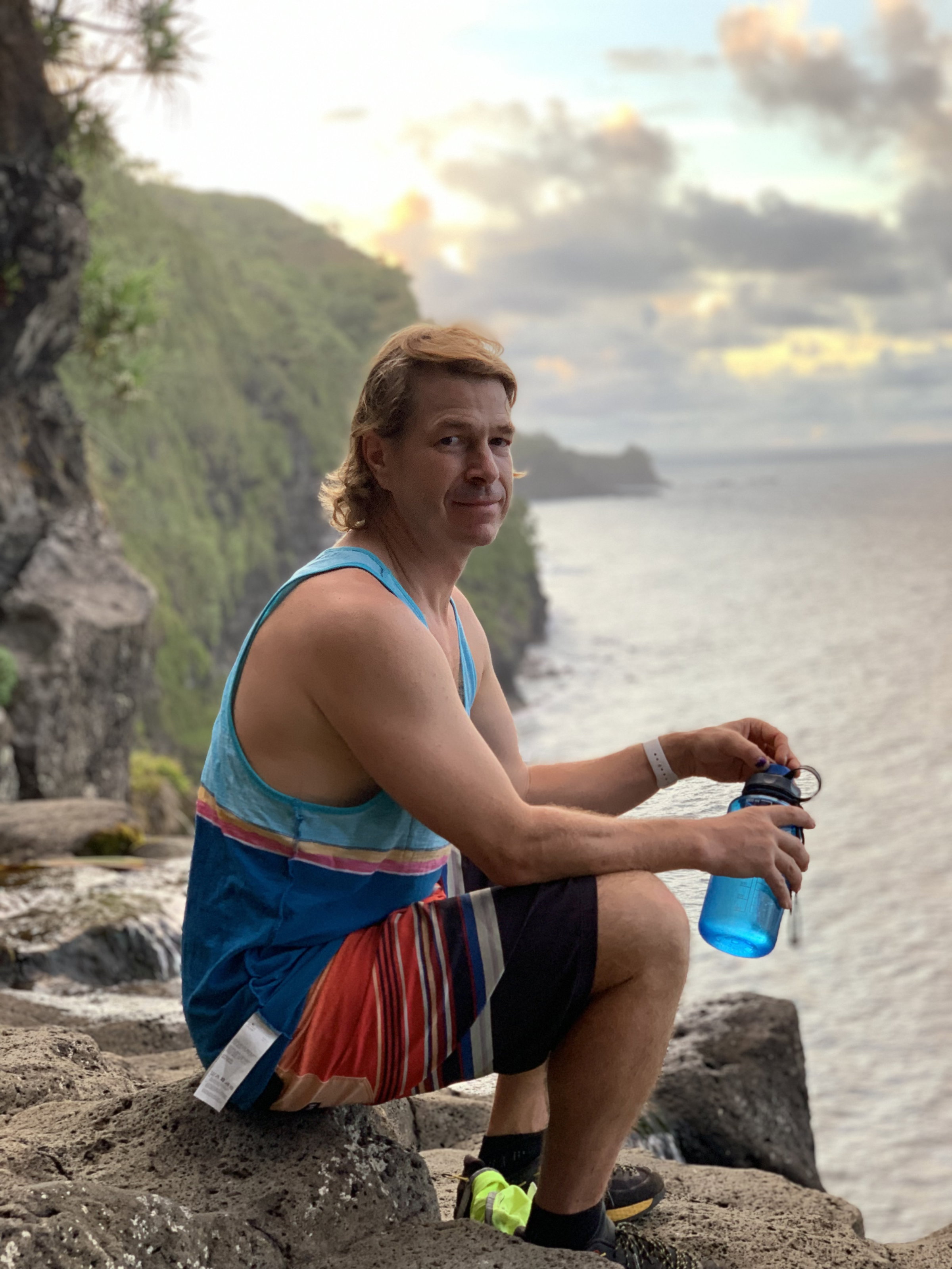 Trevor sitting on a rocky coastline at sunset